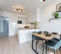 A stylish open-plan kitchen and dining area with sleek white cabinets, wooden accents, and modern decor. Bright, spacious, and fully equipped—perfect for cooking and enjoying meals in comfort.