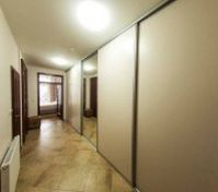 Long hallway is furnished with huge wardrobe and big mirror. 