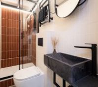 Modern bathroom with a walk-in shower, stylish black fixtures, and warm lighting. Compact but well-organized, with a heated towel rack and a spacious stone sink.
