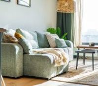 A stylish and cozy living room with a comfortable sofa, designer tables, and natural elements. Bright interior with large windows, green plants, and elegant lighting creates the perfect space to relax. Ideal for unwinding and enjoying cozy evenings.